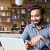 Man sitting at desk, smiling at laptop screen