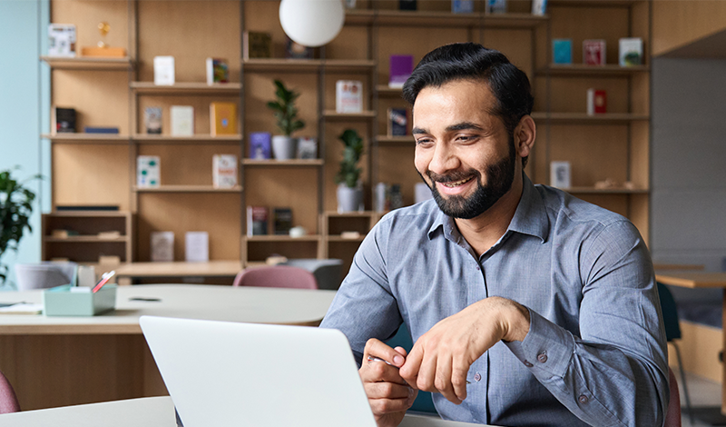 Man sitting at desk, smiling at laptop screen